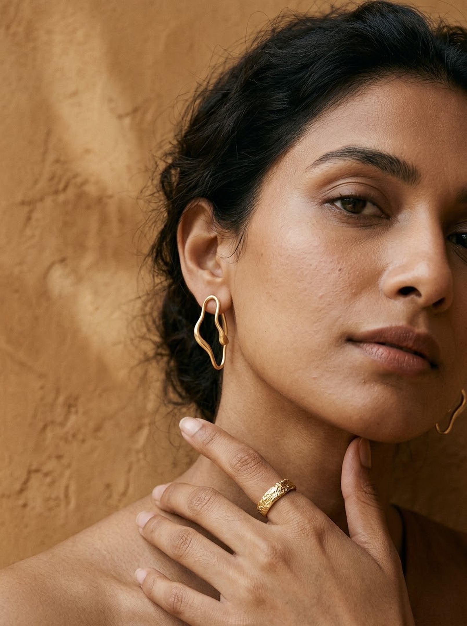 High-fashion model wearing sculptural gold contour earrings and textured ring
